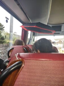 The image shows the inside of the coach bus transporting conference attendees from Killarney to Dublin after the conference. You can see the red seat back in front and a person with an open umbrella due to a leak in the roof.